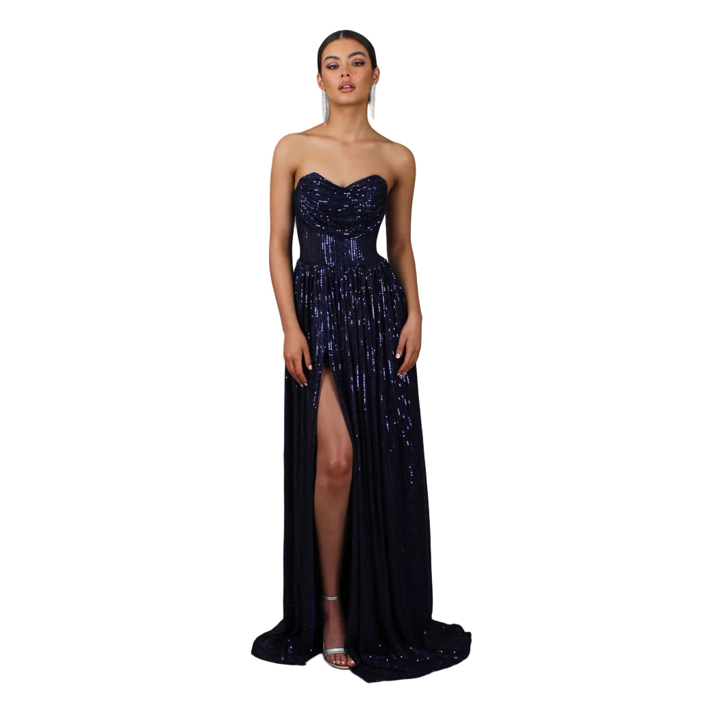 Woman wearing a strapless, sequined evening gown with a high slit on a gray background.