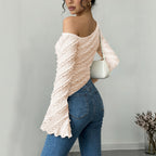 Woman wearing a light pink off-shoulder top and blue jeans against a gray background