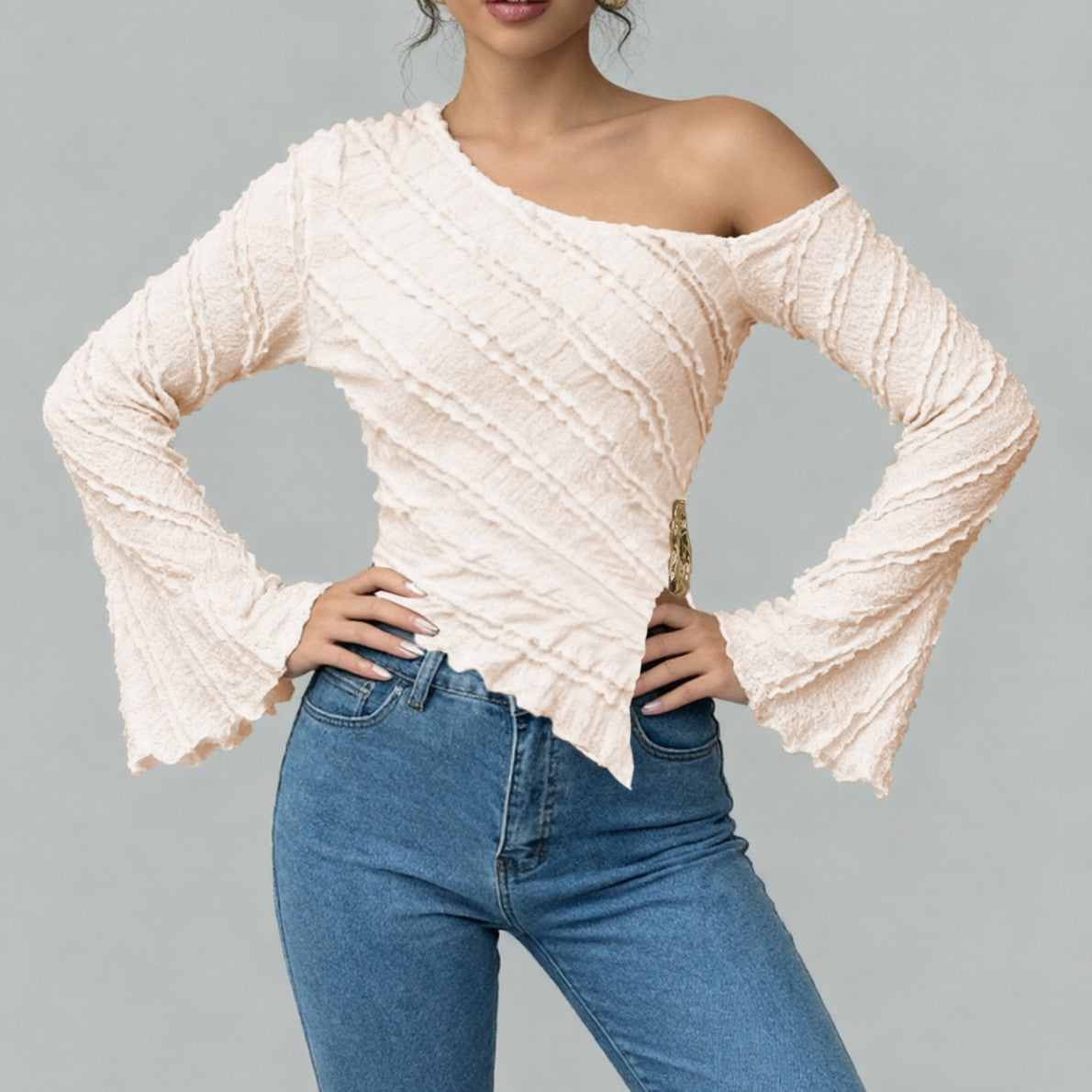 Woman wearing a beige off-shoulder top and blue jeans on a gray background