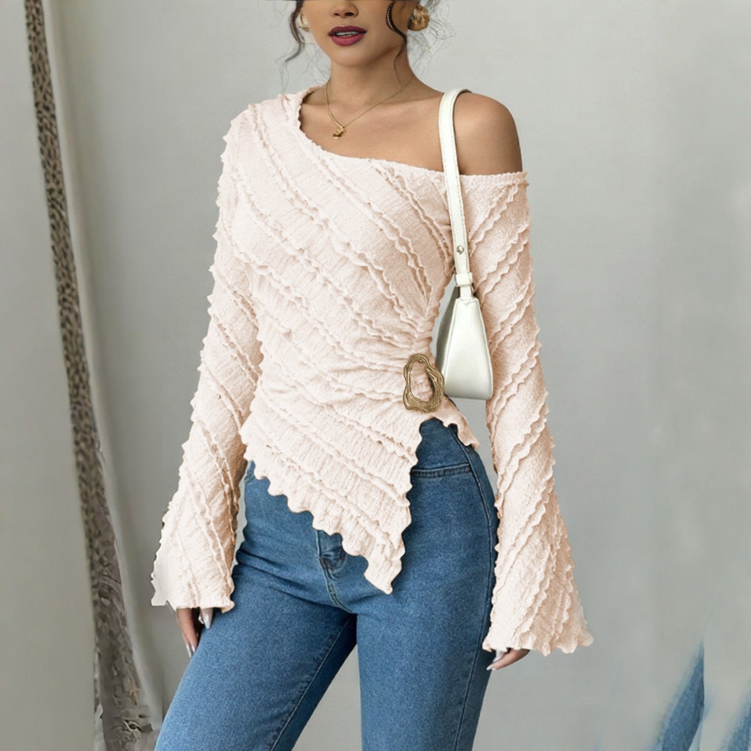 Woman wearing a beige off-shoulder sweater and blue jeans, holding a white handbag.