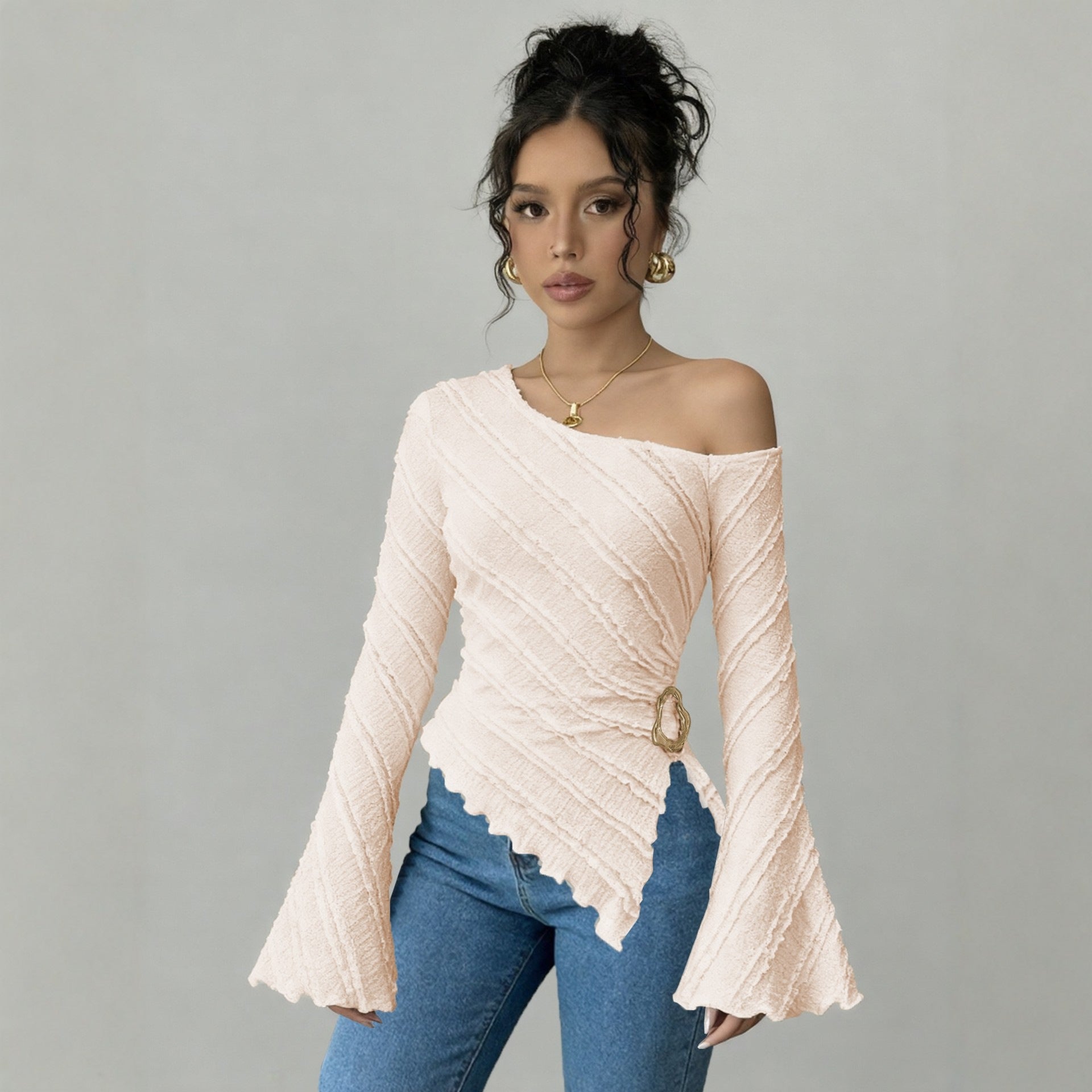 Woman wearing a pink off-shoulder top with a belt and blue jeans on a gray background