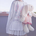 Person wearing a white dress with a cartoon design, holding a plush toy.