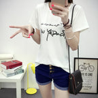 Person wearing a white t-shirt with text and blue shorts, posing in a room.