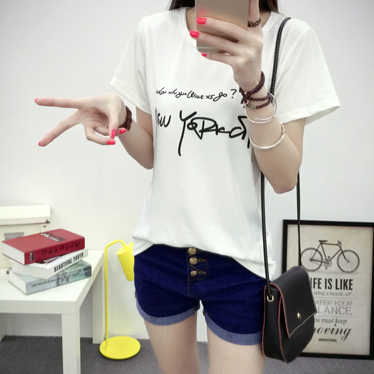 Person wearing a white t-shirt with text and blue shorts, posing in a room.