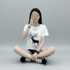 Person wearing a white t-shirt with a black deer graphic sitting on the floor.