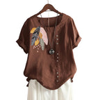Brown blouse with feather design on a hanger against a beige wall