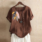 Brown blouse with feather design on a hanger against a beige wall