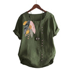 Green blouse with floral embroidery on a hanger against a beige wall