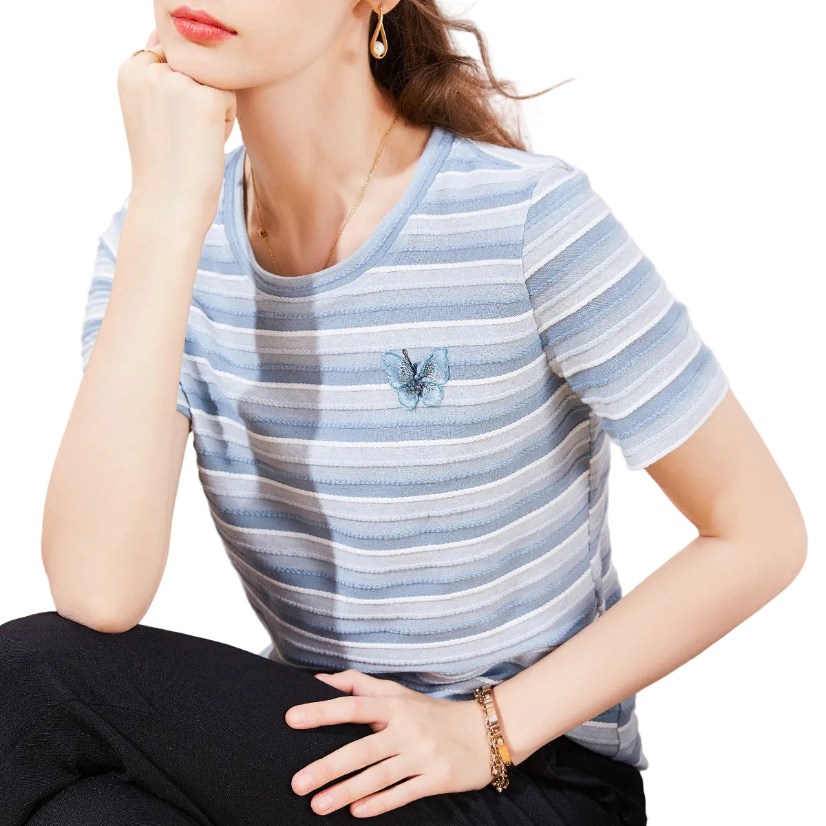 Woman wearing a blue and white striped shirt with a small emblem, sitting on a couch.
