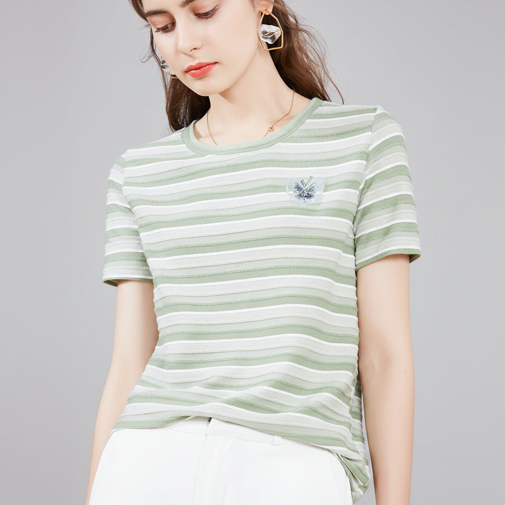 Woman wearing a green and white striped shirt with a small embroidered design.