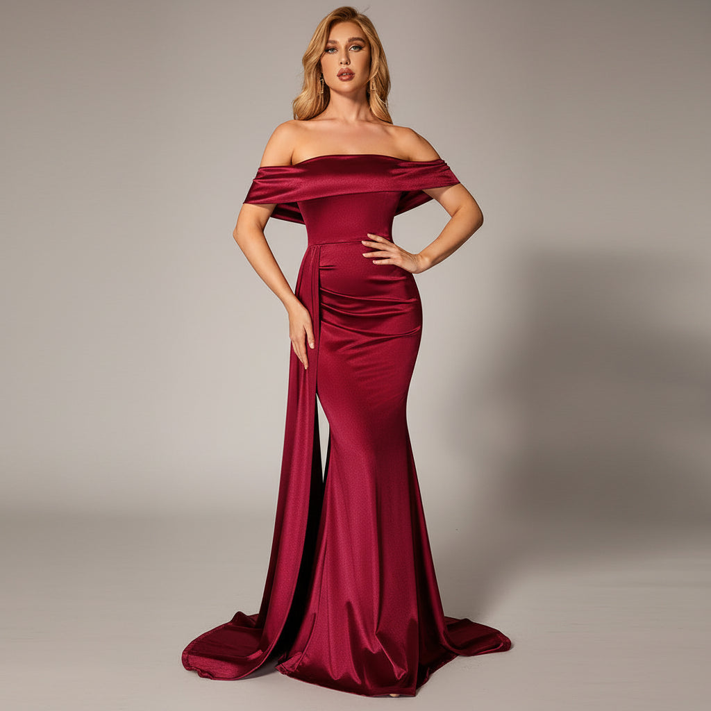 Woman in a burgundy off-shoulder gown posing against a dark background with a red couch.