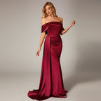 Woman in a burgundy evening gown standing against a dark background with a red couch.