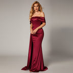 Woman in a burgundy off-shoulder gown standing against a dark background