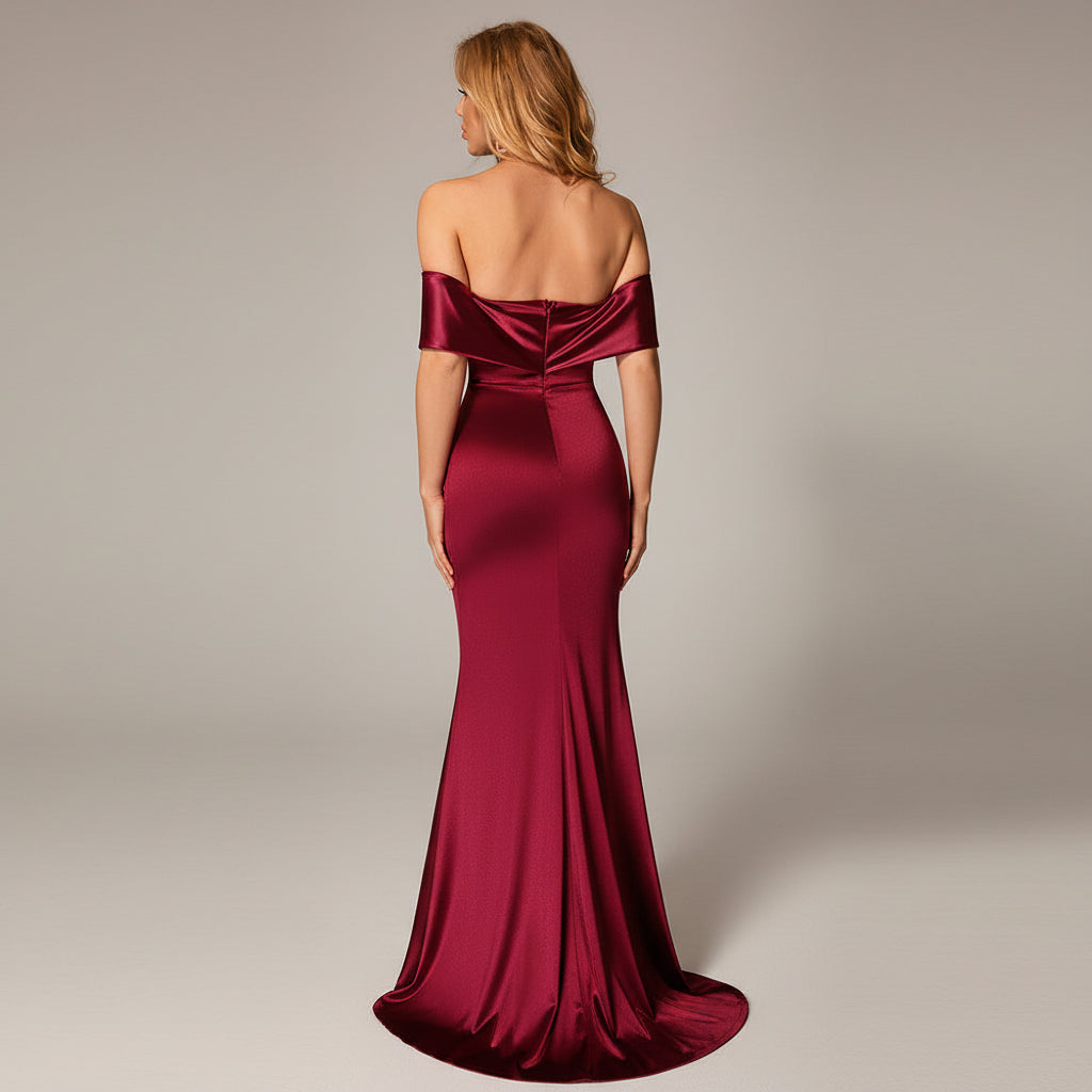 Woman in a burgundy evening gown standing in a dimly lit room with a red couch.