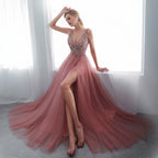 Woman in a pink evening gown with a high slit standing in a bright room.